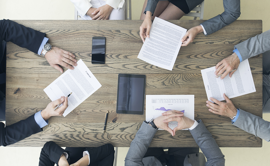Business people discuss contract sitting around office table, top view