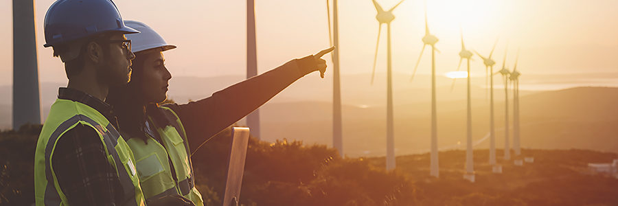 Young maintenance engineer team working in wind turbine farm at sunset