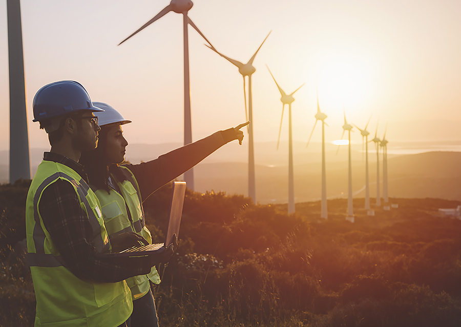 Young electrical engineer woman and business man standing in front of wind turbines checking and working about technical problems and writes the results of measurements with laptop pc in wind power plant electric energy station. xxxl size taken with canon 5d mIV