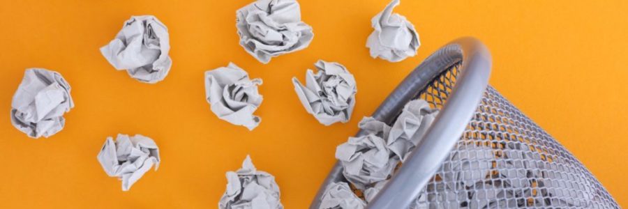 Grey crumpled paper balls rolling out of a trash can