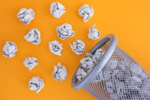 Grey crumpled paper balls rolling out of a trash can