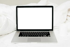 Laptop with blank white screen on white cozy bed in sunny light