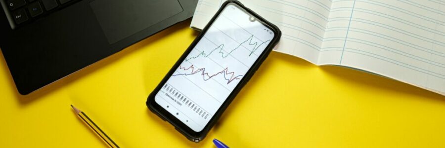 A table with a laptop, a notebook and a phone showing statistics A table with a laptop, a notebook and a phone showing statistics
